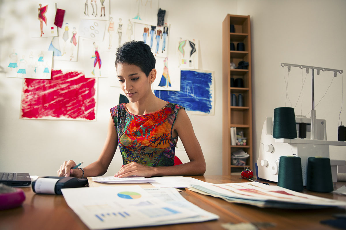 hispanic woman doing budget in fashion designer atelier Money and financial planning, young hispanic self-employed woman checking bills and doing budget with calculator, computer and papers in fashion design studio